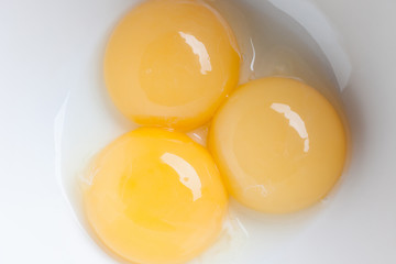 Three yellow fresh yolks separated from white in white ceramic bowl directly from above