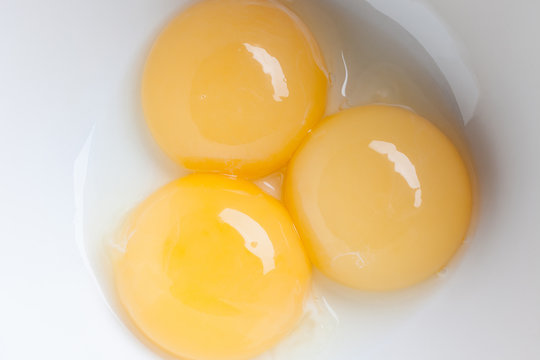 Three yellow fresh yolks separated from white in white ceramic bowl directly from above