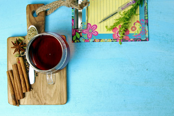 A cup of tea with spices on a wooden board with a notepad and a pen with copy space.
