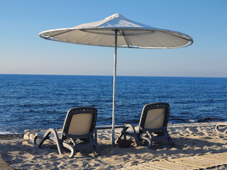 Beach chairs and umbrella on the sand near sea, blue sky