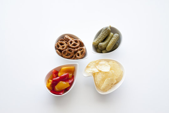 Peperoni in agrodolce, cetrioli sottaceto, bretzel, patatine in scodelle bianche su sfondo chiaro