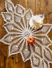 knited openwork crochet doily lying on a wooden table. view from above