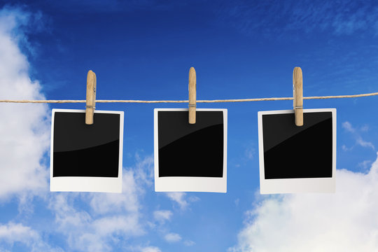 clothespin hanging with blank photo paper on blue sky background