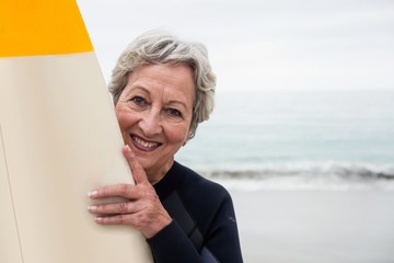 Senior woman in wetsuit holding a surfboard on the beach