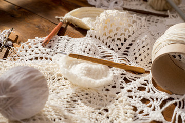 white and beige openwork crochet doily, and balls of wool on a wooden table. view from above - obrazy, fototapety, plakaty