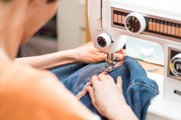 young woman sews on the sewing machine denim