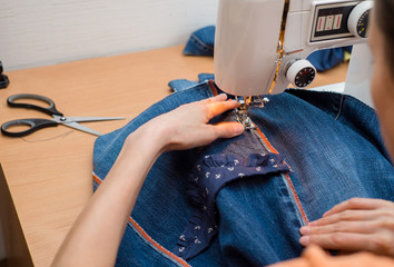 young woman sews on the sewing machine denim