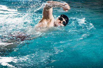 Young man swimming the front crawl in a pool