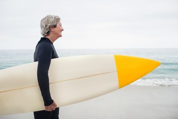 Senior woman holding surfboard on the beach