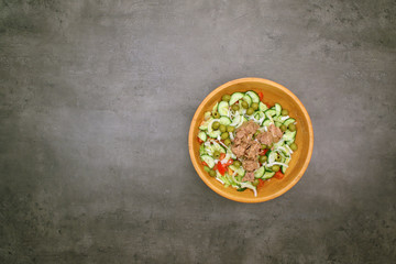 Tuna salad with pasta and vegetables. Top view of wooden bowl on grey kitchen table. 