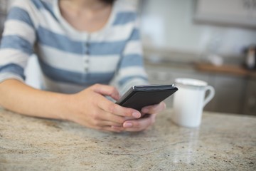 Woman typing a text message on her mobile phone in kitchen