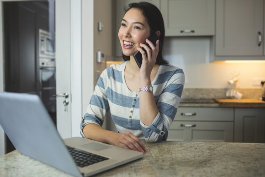 Happy woman using laptop while on call 