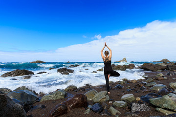 Summer yoga session on beautiful Playa de Roque de Las Bodegas with giant rock and high waves - tropical Tenerife island, Canary in Spain. Vriksha-asana, tree pose
