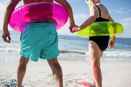 Senior couple in inflatable ring walking towards sea