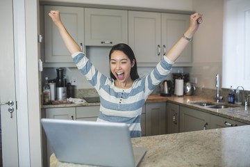 Fototapeta na wymiar Excited woman using a laptop in the kitchen