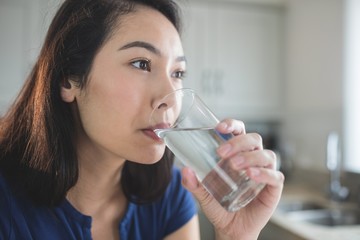 Young woman drinking a glass of water in kitchen
