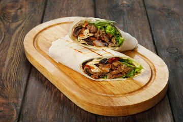 Burrito with pork meat and vegetables at wood desk