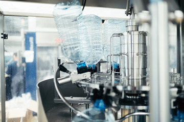 Robotic factory line for processing and bottling of pure spring water into canisters and bottles. Unrecognizable worker in background. Selective focus.