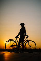 beautiful hipster girl with a bicycle on the road during sunset