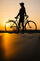  hipster girl with a bicycle on the road during sunset