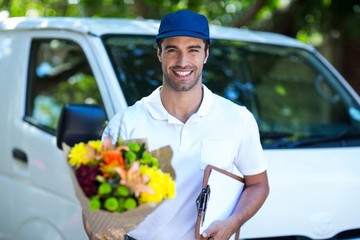Smiling delivery man holding flower bouquet and clipboard 