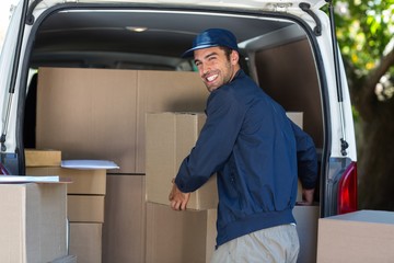 Happy delivery man loading cardboard box in van