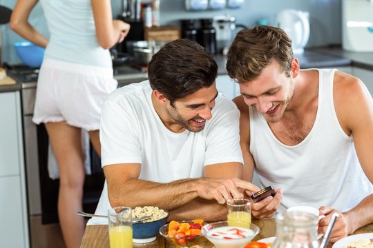 Happy men using mobile phone while having breakfast
