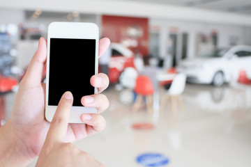 hands holding mobile phone with new cars in showroom
