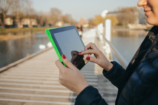 Smiling young woman, student taping on tablet ,using tablet in a city park near river.Young smiling student outdoors with tablet.Life style.City