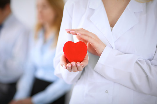 Femail doctor holding a red heart in his hands on a background of the patient. Health care concept