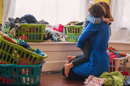 Mother hugging son in living room surrounded by laundry