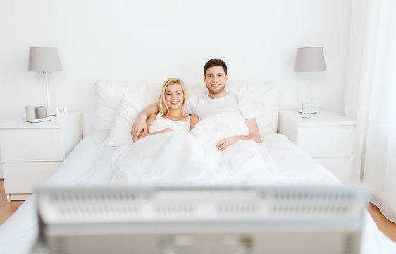 Happy Couple Lying In Bed At Home And Watching Tv