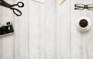 Work desk with free space for text. Coffee, camera, scissors, notepad, pencil, glasses on wooden table. Top view.