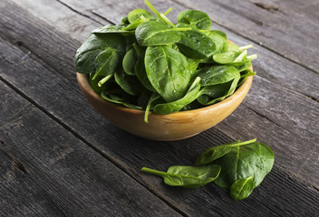 Spinach leaves in bowl on dark wooden background
