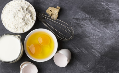 Ingredients for pastries: flour, eggs, milk against a dark backg