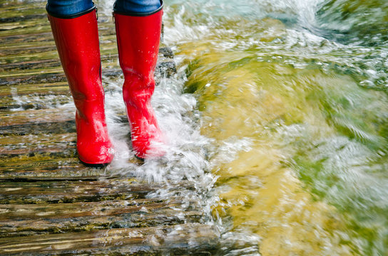 red rubber boots in water on wooden bridge, river overflowed its banks.
