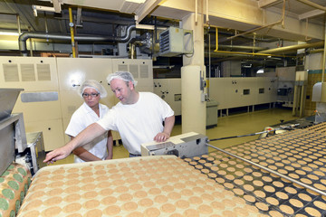 Germany, Saxony-Anhalt, two workers at production line with cookies in a baking factory