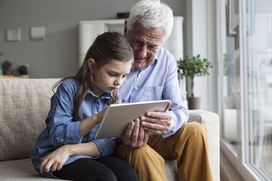 Grandfather and his granddaughter sitting together on the couch using digital tablet