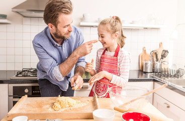 Happy father and daughter preparing cookie dough in the kitchen - obrazy, fototapety, plakaty