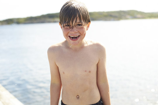 Sweden, Orust, laughing wet boy standing in front of the sea