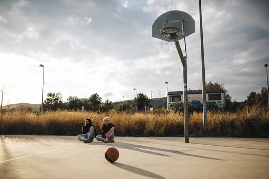 Two young men sitting on outdoor basketball court