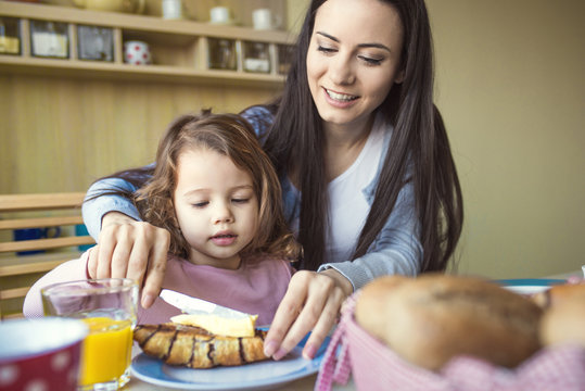 Portrait of mother and her little daughter together at breakfast table