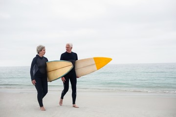 Senior couple with surfboard walking on the beach