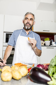 Austria, Man in kitchen eating carrot
