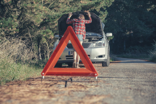 Young woman examining damaged car with a warning triangle in the road