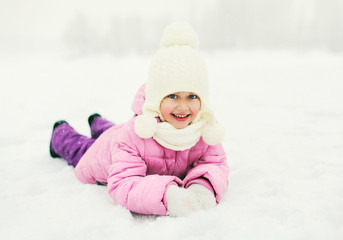Fototapeta na wymiar Happy smiling little girl child lying on snow in winter day