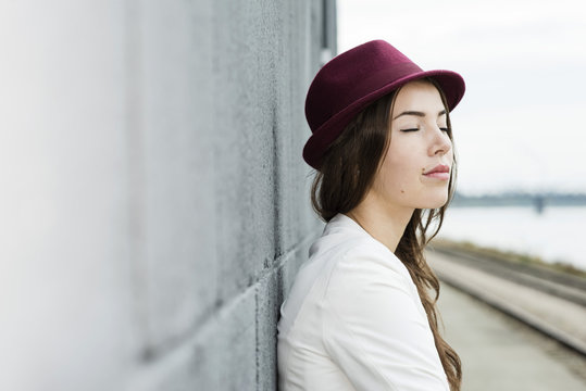 Portrait of young woman with closed eyes wearing hat leaning against a wall