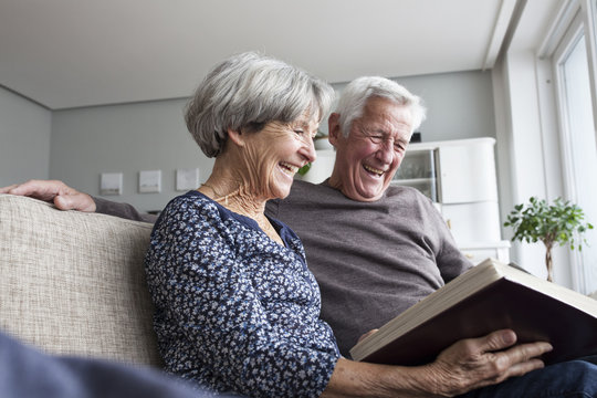 Laughing senior couple sitting on the couch at living room watching photo album