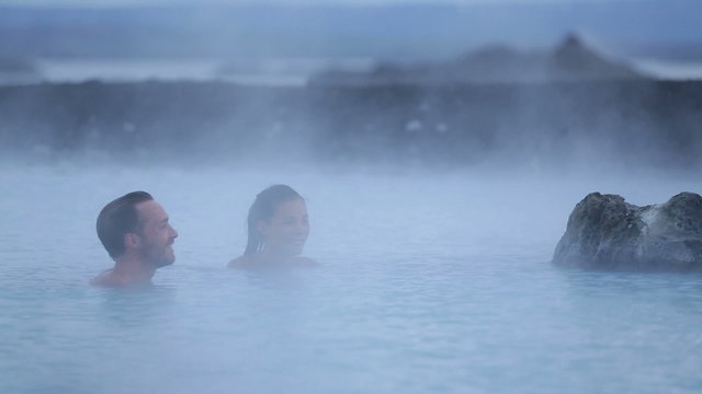 Hot spring geothermal spa on Iceland. Romantic couple in love relaxing in hot pool on Iceland. Young woman and man enjoying bathing relaxed in a blue water lagoon Icelandic tourist attraction. Sunset.