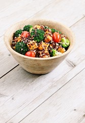 Quinoa salad with broccoli,sweet potatoes and tomatoes on a rustic wooden table.Superfoods concept.Selective focus. 